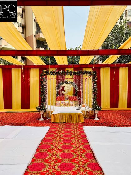 A wide view of the outdoor Kirtan setup. The entire area is covered with a canopy of yellow drapes, and a red carpet leads to the beautifully decorated stage, creating a complete devotional environment.