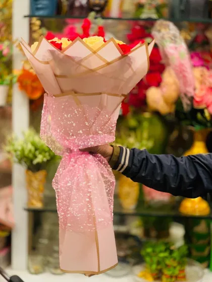 A tall bouquet of red and yellow roses wrapped in shimmering pink paper. This shows how the wrapping style can add height and drama to an arrangement.