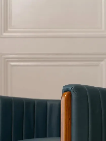 The elegant silhouette of the accent chair against a classic paneled wall. The deep blue leather and warm wood create a timeless look that exudes sophistication.