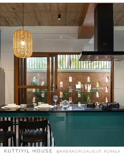 The kitchen at Kuttiyil House shows how a pop of color can transform a space. The glossy teal cabinetry contrasts with the patterned backsplash and exposed concrete ceiling, creating a modern kitchen that is both functional and full of personality.