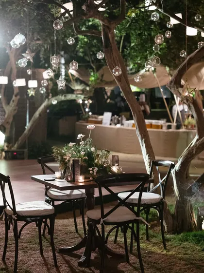 A cozy seating nook under trees filled with hanging lanterns and glass baubles. We create smaller, intimate spaces within a larger event for guests to have quiet conversations.