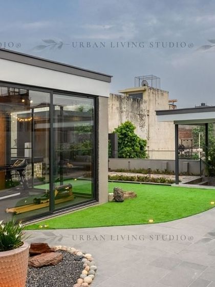 A view of the Aligarh penthouse project, showing the connection between the indoor gym space and the outdoor landscape. The design uses curved pathways and planters to create a natural, flowing feel.