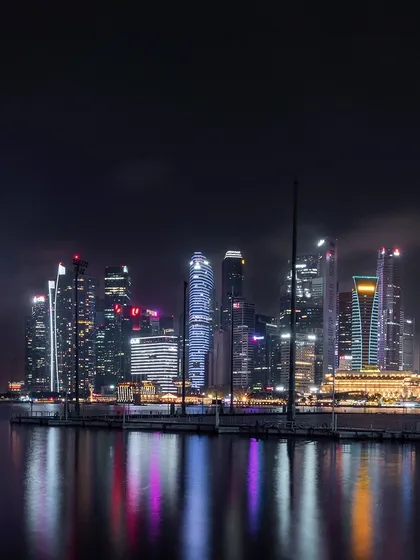 A view of Singapore's central business district at night, with the city lights reflecting on the water in the foreground.