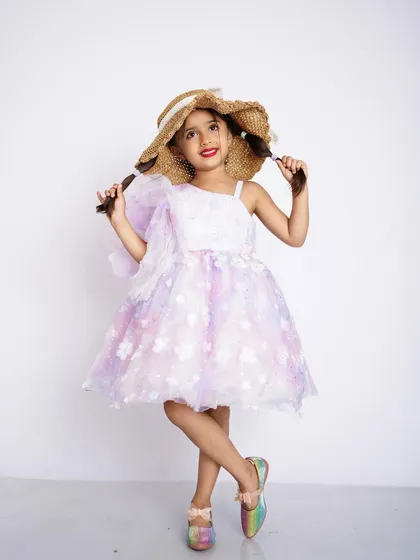 A full-length studio portrait of a young girl in a lovely floral dress and straw hat, posing with pigtails.