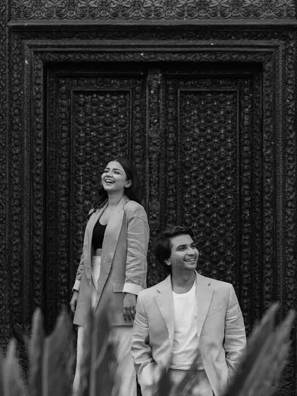A moment of shared laughter in front of an intricately carved wooden door. This black and white candid shot highlights the couple's genuine connection, framed by the rich heritage of their surroundings.
