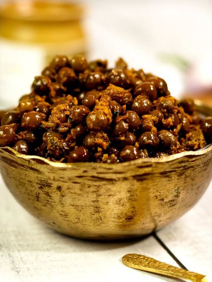A close-up shot of the "Teet Ka Achaar" in a vintage brass bowl. The focus is on the texture and rich, dark color of the pickle, making it look incredibly flavorful.