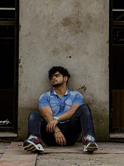 A full shot capturing a relaxed, contemplative pose against a concrete wall. The urban setting and casual styling make this a great addition to a street style portfolio.