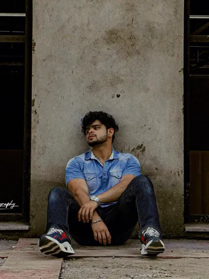 A full shot capturing a relaxed, contemplative pose against a concrete wall. The urban setting and casual styling make this a great addition to a street style portfolio.
