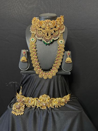 This antique bridal set features a wide, ornate choker that makes a bold statement. It is paired with a matching long necklace and vaddanam to complete the majestic look.