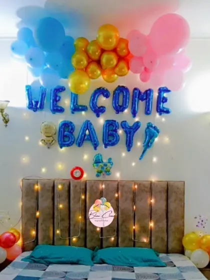 A colorful 'Welcome Baby' bedroom decoration with blue, pink, and gold balloons over the bed, complemented by fairy lights.