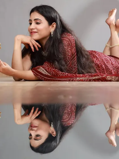 A creative studio shot using a reflective floor to capture this beautiful bandhani-style saree. The model's pose with the antique-style mirror adds a touch of vintage charm and artistry.