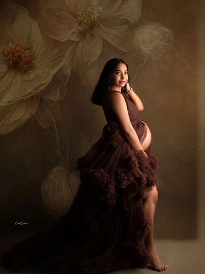 A fine-art portrait with a painterly floral background. The mom-to-be looks stunning in a deep brown ruffled gown.