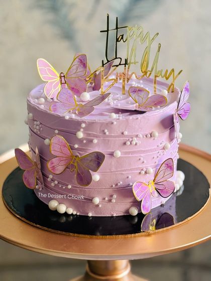 A lovely tall cake in a soft purple hue, adorned with delicate paper butterflies and pearls for a whimsical, dreamy effect.