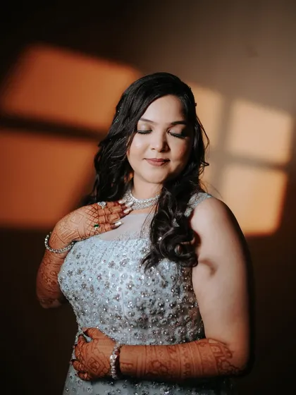 A moment of quiet reflection for the bride. The warm light catches the intricate details of her gown and the beautiful henna on her hands, capturing her glow before the engagement festivities.