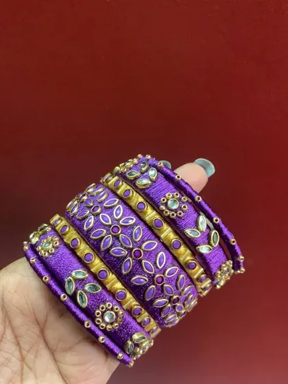 A detailed view of a custom bridal bangle set in purple, showcasing intricate floral embroidery work with silk thread and sparkling kundan stones.