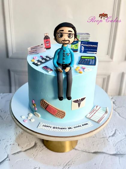 A custom cake for a pharmacist. The design is decorated with all sorts of edible medical supplies, including pills, prescription pads, and medicine boxes, topped with a fondant figure of the doctor.