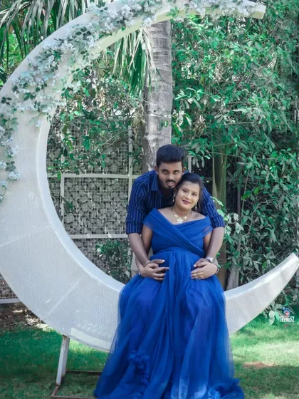 A romantic portrait of a couple seated on a large, crescent moon prop. This set is perfect for creating magical, fairytale-like maternity photos under a canopy of green.