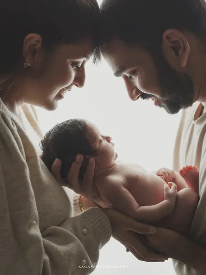 A beautiful high-key portrait of new parents gazing lovingly at their baby, held between them. The soft, bright light creates a dreamy and angelic feel.