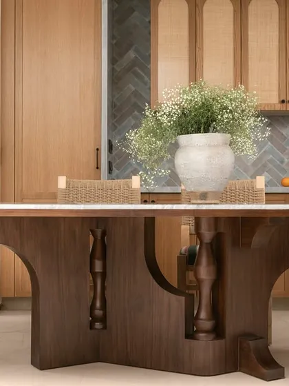 The dining area in our 'Kolam Pop' home features a table with a sculptural wooden base and lathe-turned accents. It's paired with woven chairs and a patterned bench, celebrating artisanal heritage with a modern twist.