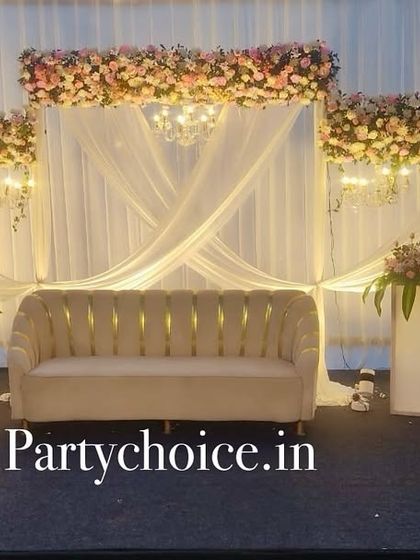 An elegant outdoor engagement stage at dusk. The white drapes, floral headers, and chandeliers create a magical and romantic atmosphere.