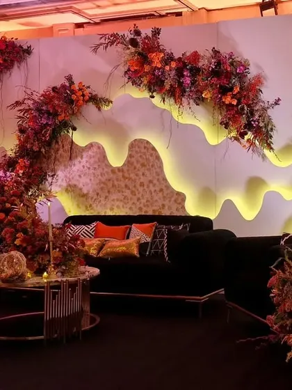 A lounge area designed for the burnt orange themed cocktail night. A custom-fabricated backdrop with organic, glowing cutouts is paired with black velvet sofas and autumnal floral arrangements.