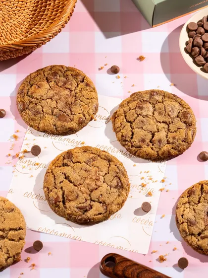 Freshly baked chocolate chip cookies. The scattered chocolate chips and brown sugar create a scene of delicious messiness.