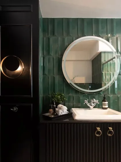 A close-up of the master bathroom's details: a fluted black vanity, a round LED mirror, and rich emerald green tiles.