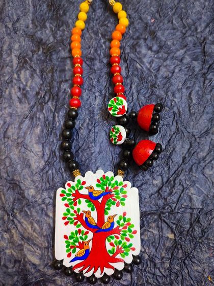 This hand-painted necklace depicts a tree of life, a central theme in Gond art. The tree is filled with small birds, symbolizing community and nature's abundance. It's a rustic and meaningful piece.