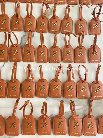 A closer look at our personalized luggage tags, ready for a large group trip. Each tan leather tag is customized with a name and an airplane charm.