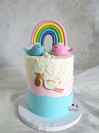 A unique and pretty baby shower cake with a stork, rainbow, and two little birds on top.