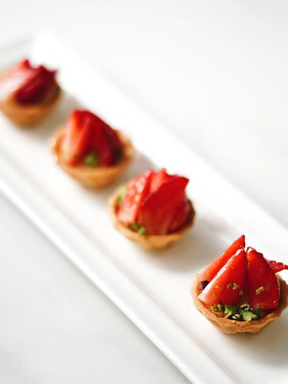 A row of mini strawberry tartlets, ready for a party. These bite-sized desserts are easy for guests to enjoy while mingling.