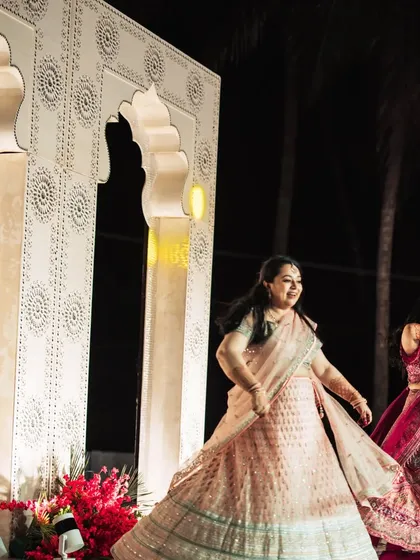 A lively Sangeet performance on stage. The backdrop features intricately designed white arches, adding a touch of Mughal-inspired elegance to the energetic dance night.