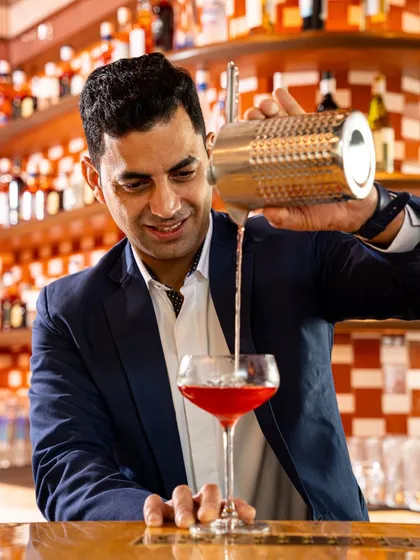 He’s not just behind the bar, he’s behind the brilliance of every pour. Say hello to Varun, our award-winning mixologist, as he crafts a vibrant red cocktail.