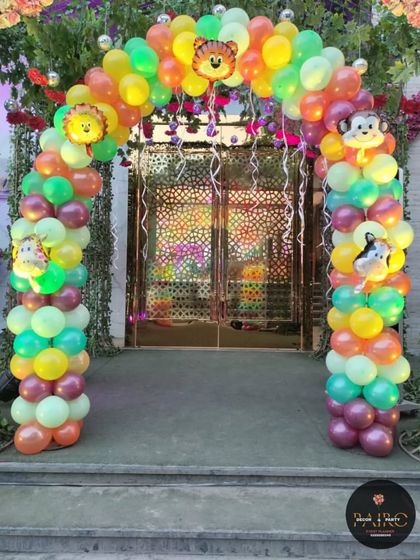 A jungle-themed entrance arch for a first birthday. The arch is made of colorful balloons and decorated with cute animal face foil balloons to welcome guests.