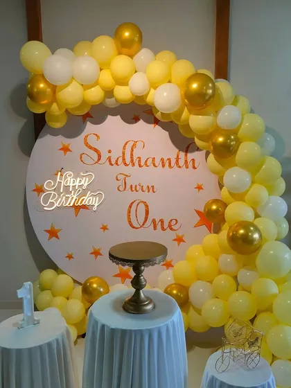 A sunny yellow and white balloon arch against a custom circular backdrop for a first birthday.