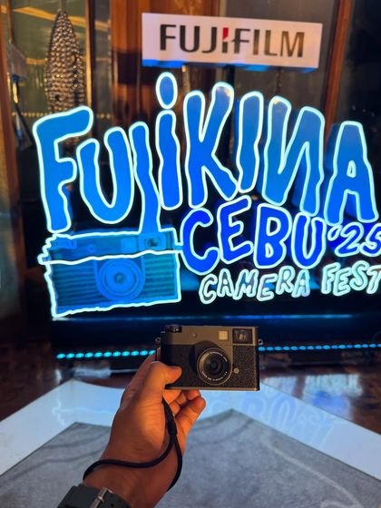 A close-up of the Fujifilm X half camera against the neon sign of the Fujikina event. This is a creative product shot that highlights the camera as the star of the show.