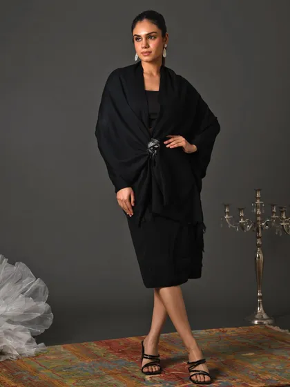 An all-black look styled for a festive campaign, featuring a draped shawl secured with a statement brooch. This showcases how accessories can transform a simple dress into a sophisticated and elegant outfit.