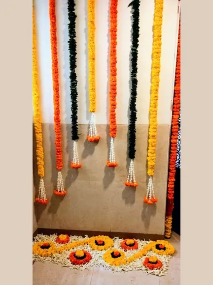 This simple yet elegant entrance decor features hanging garlands of marigolds and tuberoses, with a small floral rangoli at the base, perfect for a wedding hall or home entrance.