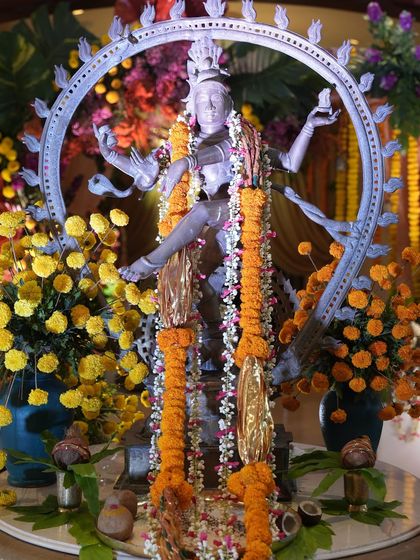 A closer look at the Nataraja statue, adorned with a long marigold garland. The vibrant yellow and orange flowers create a beautiful contrast with the brass idol, highlighting its divine form.