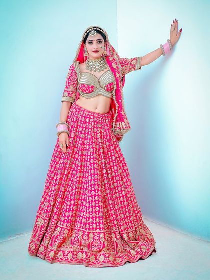 A full-length shot of the bride against a clean, simple background. This studio-style portrait puts all the focus on her vibrant pink lehenga and confident pose.