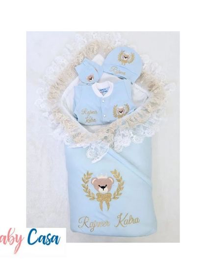 A personalized coming home set for "Rajveer Kalra." This teddy bear themed collection in blue and gold includes a wrap with lace trim and a matching romper for a charming look.