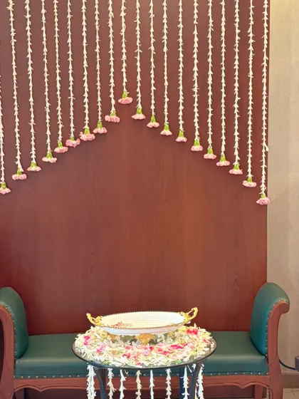 This simple and elegant setup features a backdrop of hanging floral strings, creating a perfect photo spot. The bowl of floating flowers on the table adds another beautiful, traditional touch.