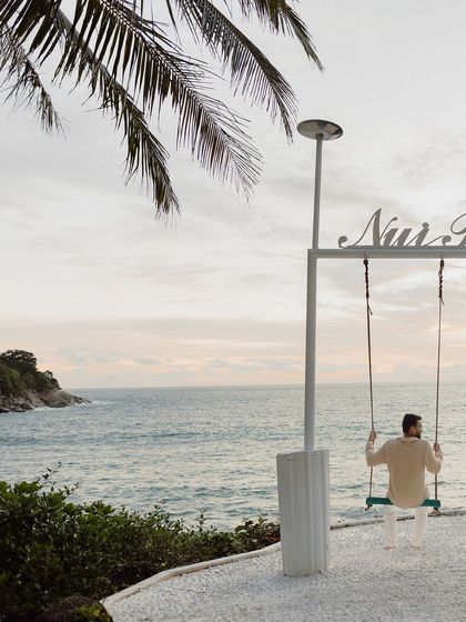 A solo portrait of the groom on the Nui Beach swing, looking out at the ocean.
