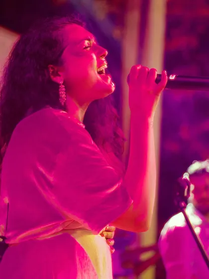 Dhruvi delivering a powerful vocal performance during a wedding reception. The pink lighting and her passionate expression capture the vibrant mood we create.