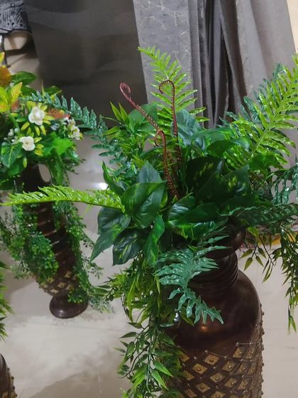 A close-up of one of the artificial fern arrangements in a decorative vase. The different leaf shapes and textures make the arrangement look very natural.