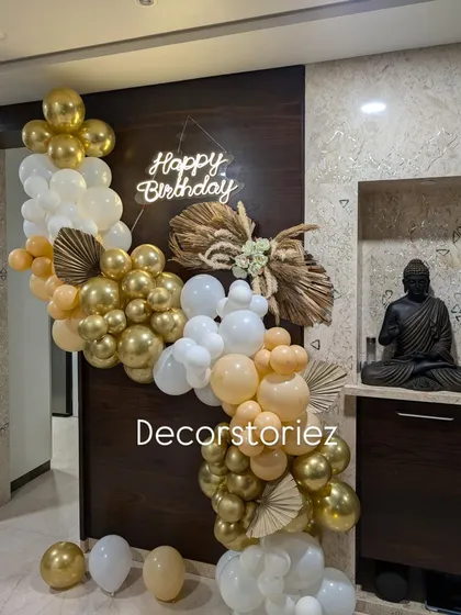 For a more sophisticated celebration, I design trendy boho-themed decor. This setup combines an organic cascade of chrome gold, white, and nude balloons with dried pampas grass and palm spears, all highlighted by a warm neon birthday sign.