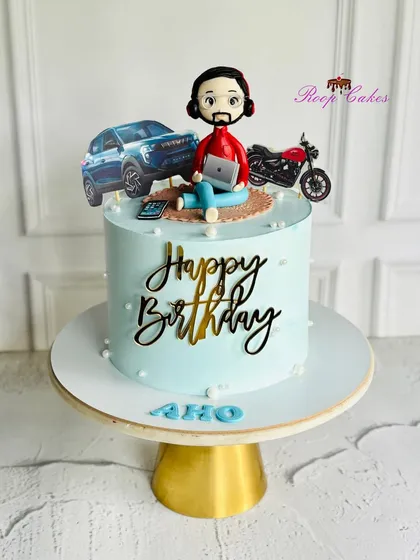 A custom cake for a husband, featuring a fondant figurine chilling with his laptop, with his favorite car and bike right beside him.