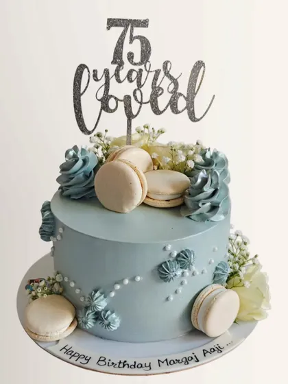 A lovely pastel blue cake for a 75th birthday, topped with macarons and delicate flowers. The "75 years loved" topper makes it extra special.