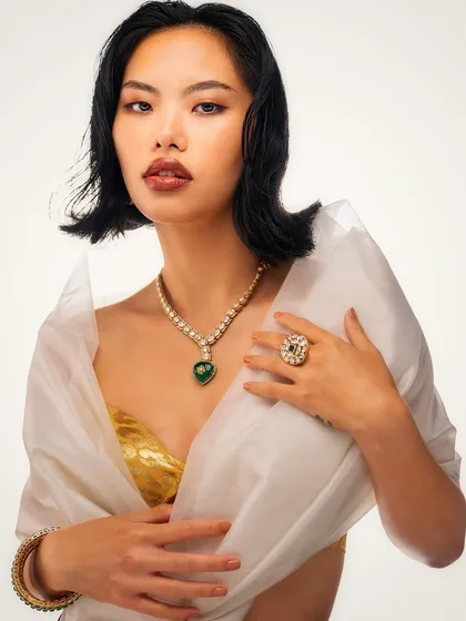 A timeless jewelry portrait. The lighting is focused on bringing out the brilliance of the emerald necklace and the soft glow of the pearls, set against a clean, high-key background for maximum impact.
