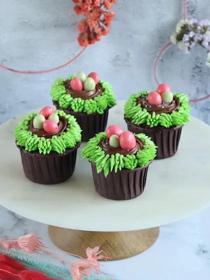 Easter treats in a bite. Our chocolate cupcakes are decorated with green frosting "grass" and candy eggs, perfect for an Easter celebration.
